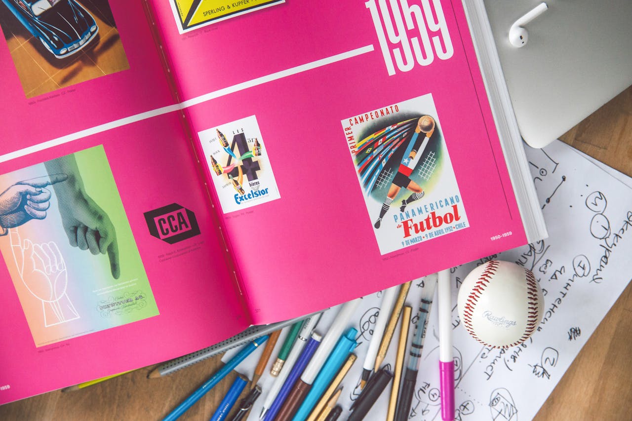 Home Artistic workspace featuring an open design book, sketches, pens, and a baseball on a desk.